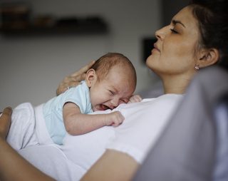 mujer con cara cansada con un bebe encima que llora
